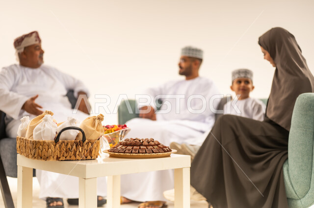 تجمع العائلة العمانية لاستقبال العيد المبارك, إظهار مشاعر الحنان والمحبة, الجلوس في غرفة المعيشة في جو عائلي دافئ، بورتريه لعائلة عربية خليجية عمانية تحتفل بالمناسبات الاسلامية برفقة بعضها البعض, تقديم الضيافة والحلوى ، ارتداء الثياب الجديدة الجميلة ، خلفية بيضاء .