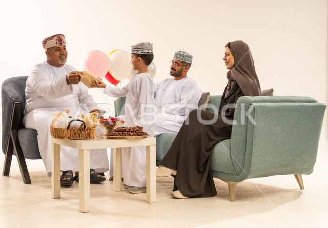 الضيافة وحسن الاستقبال ، مشاركة اجواء رائعة لعائلة عمانية داخل المنزل تحتفل بعيد الفطر السعيد ، الزيارات العائلية وتجمعات الأسر ، تقديم العيديات و الحلوى ، بورتريه لعائلة عربية خليجية عمانية تحتفل بالأعياد الإسلامية, خلفية بيضاء .