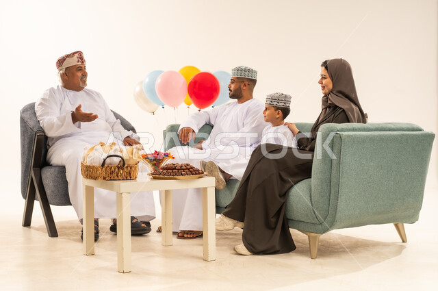 تقديم العيديات و الحلوى ، مشاركة اجواء رائعة لعائلة عمانية داخل المنزل تحتفل بعيد الفطر السعيد ، الضيافة وحسن الاستقبال ، الزيارات العائلية وتجمعات الأسر ، بورتريه لعائلة عربية خليجية عمانية تحتفل بالأعياد الإسلامية, خلفية بيضاء .