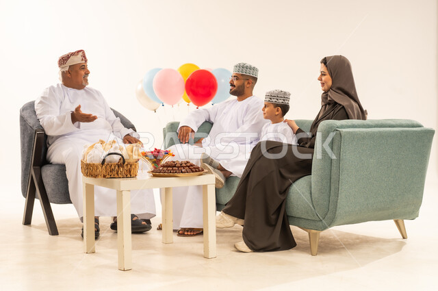 مشاركة اجواء رائعة لعائلة عمانية داخل المنزل تحتفل بعيد الفطر السعيد ، عيد فطر مبارك ، الزيارات العائلية وتجمعات الأسر ، تقديم العيديات و الحلوى ، بورتريه لعائلة عربية خليجية عمانية تحتفل بالأعياد الإسلامية, خلفية بيضاء .