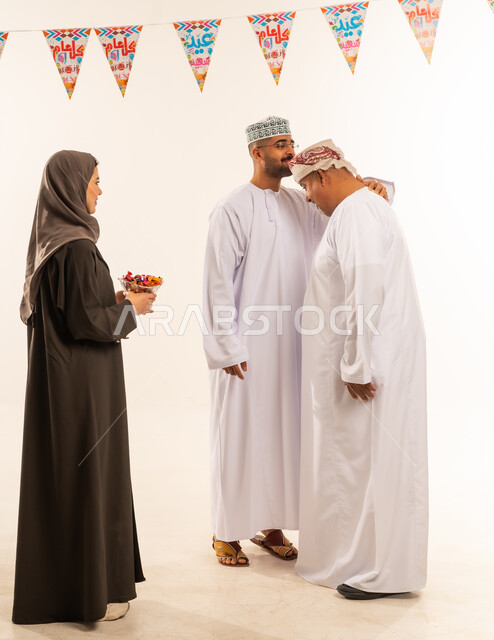 ديكورات وزينة رمضانية ، السلام وتقبيل رأس الجد والتهنئة بقدوم العيد, إظهار مشاعر المودة والمحبة العائلية, أجواء البهجة والسعادة والاحتفال, بورتريه لعائلة عربية خليجية عمانية تحتفل بالأعياد الاسلامية, امراة عربية خليجية عمانية تقدم الضيافة فى العيد ، صورة الجسم بالطول الكامل ، خلفية بيضاء.