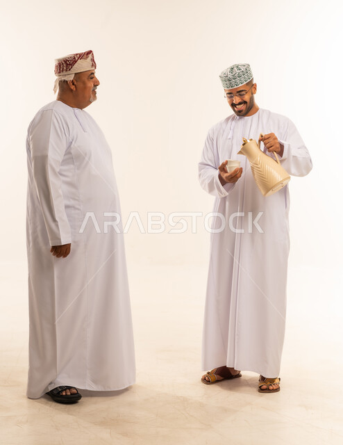 بهجة وفرحة العيد, حسن استقبال واكرام الضيوف, العيد بين الاهل , مناسبات واعياد اسلاميه, تقديم الضيافة العربية ، زيارات وتجمعات عائليه, ايماءات الفرحة والسرور والسعادة بالاحتفاليات, رجل عربي عماني خليجي يقدم الضيافة لوالده ، صورة الجسم بالطول الكامل ، خلفية بيضاء .