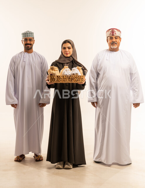 مشاعر المودة والمحبة بين الاهل ، المعايدات والتهنئات وطقوس المناسبات الاسلامية، النظر الى الكاميرا بايماءات الفرحة والسرور والسعادة بالاحتفاليات , حسن استقبال واكرام الضيوف, بورتريه لعائلة عربية عمانية خليجية ترتدي الزى العمانى التقليدي ، صورة الجسم بالطول الكامل ، خلفية بيضاء .