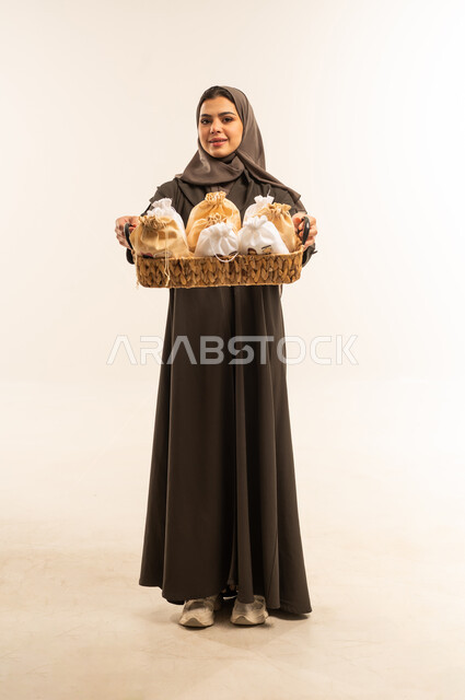 اجواء العيد فى سلطنة عمان ، مشاعر المودة والمحبة بين الاهل ، المعايدات والتهنئات وطقوس المناسبات الاسلامية، النظر الى الكاميرا بايماءات الفرحة والسرور والسعادة بالاحتفاليات , حسن استقبال واكرام الضيوف, بورتريه لامرأة عربية عمانية خليجية ترتدي العباءة والحجاب ، صورة الجسم بالطول الكامل ، خلفية بيضاء .