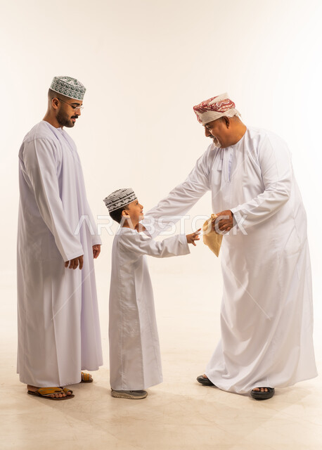 تقوية وتعزيز الروابط الأسرية، السلام و التهنئة بقدوم العيد, أجواء البهجة والسعادة والاحتفال, بورتريه لعائلة عربية خليجية عمانية تحتفل بالأعياد الاسلامية وتتبادل المعايدات, تقديم العيش و الحلوى فى العيد ، صورة الجسم بالطول الكامل ، خلفية بيضاء.