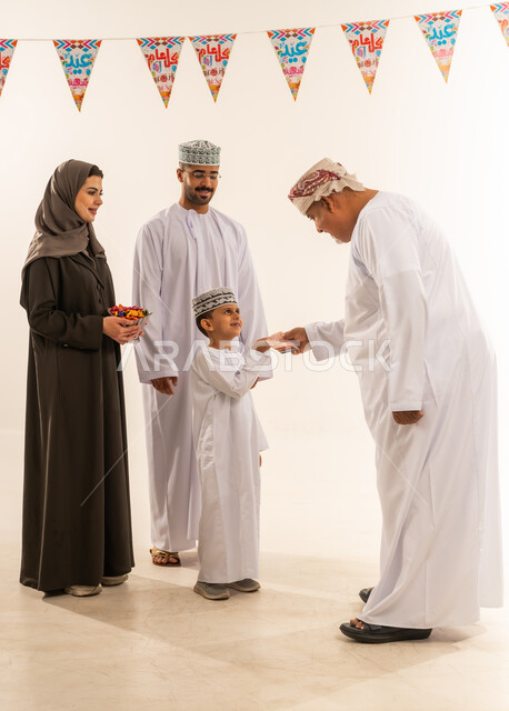 التهنئة بقدوم العيد, ديكورات وزينة رمضانية ، أجواء البهجة والسعادة والاحتفال, إظهار مشاعر المودة والمحبة العائلية,  بورتريه لعائلة عربية خليجية عمانية تحتفل بالأعياد الاسلامية ، تقديم العيش والحلوى فى العيد ، خلفية بيضاء.