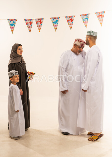 السلام وتقبيل رأس الجد والتهنئة بقدوم العيد, ديكورات وزينة رمضانية ، إظهار مشاعر المودة والمحبة العائلية, أجواء البهجة والسعادة والاحتفال, بورتريه لعائلة عربية خليجية عمانية تحتفل بالأعياد الاسلامية, خلفية بيضاء.