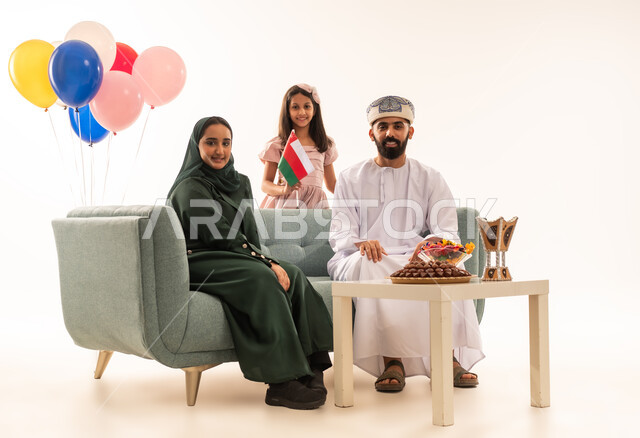 الزيارات العائلية وتبادل التهنئات والمعايدات بين أفراد الأسرة بإيماءات الفرح والسرور, بورتريه لعائلة عربية خليجية عمانية تحتفل بالعيد السعيد, تقديم الحلويات والضيافة الشعبية، طقوس الأعياد والمناسبات الاسلامية في سلطنة عمان ، خلفية بيضاء .