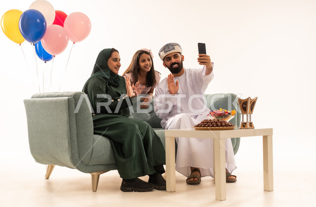 القاء التحية واجراء مكالمات الفيديو ، الزيارات العائلية وتبادل التهنئات والمعايدات بين أفراد الأسرة بإيماءات الفرح والسرور, بورتريه لعائلة عربية خليجية عمانية تحتفل بالعيد السعيد, تقديم الحلويات والضيافة الشعبية، طقوس الأعياد والمناسبات الاسلامية في سلطنة عمان ، خلفية بيضاء .