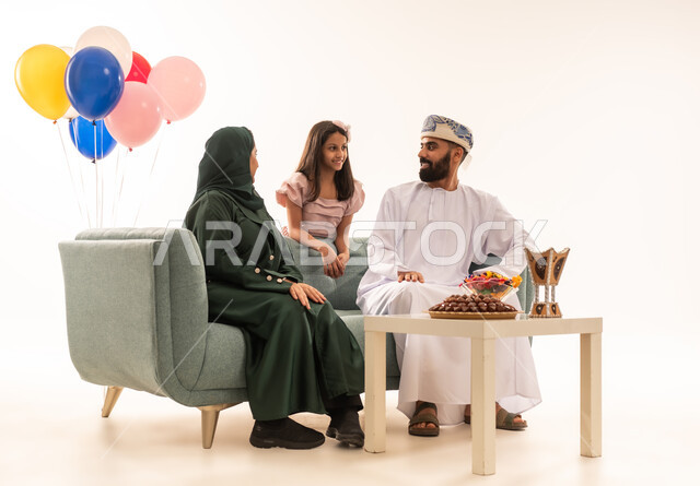 Showing feelings of love and affection, rituals of Islamic holidays and occasions in the Sultanate of Oman, a warm family atmosphere, a portrait of an Omani Gulf Arab family celebrating the happy Eid, family visits and exchanging congratulations and greetings between family members with gestures of joy and happiness, offering sweets and popular hospitality, white background.
