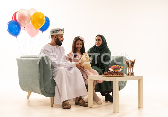 ارتداء الأزياء العمانية التقليدية الجديدة ، مفهوم الكرم وتقديم الضيافة العربية،طقوس الاحتفالات والمناسبات السعيدة في سلطنة عمان، جو البهجة والفرح والزينة، بورتريه لعائلة عربية خليجية عمانية تحتفل بالعيد المبارك، توزيع الحلويات الشعبية في الأعياد، خلفية بيضاء .