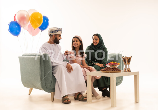توزيع الحلويات الشعبية في الأعياد، طقوس الاحتفالات والمناسبات السعيدة في سلطنة عمان، جو البهجة والفرح والزينة، بورتريه لعائلة عربية خليجية عمانية تحتفل بالعيد المبارك، ارتداء الأزياء العمانية التقليدية، مفهوم الكرم وتقديم الضيافة العربية، خلفية بيضاء .