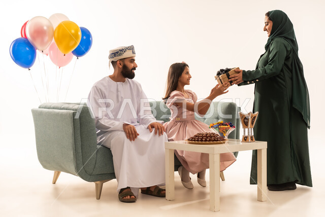 ايماءات الرضا والسرور، الألفة والمودة بين أفراد الأسرة العمانية ، بورتريه لزوجة عربية خليجية عمانية تقدم الهدية لطفلتها ، مشاركة وتقديم الهدايا بالمناسبات وأعياد الميلاد, الاجتماعات والاحتفالات العائلية، خلفية بيضاء .