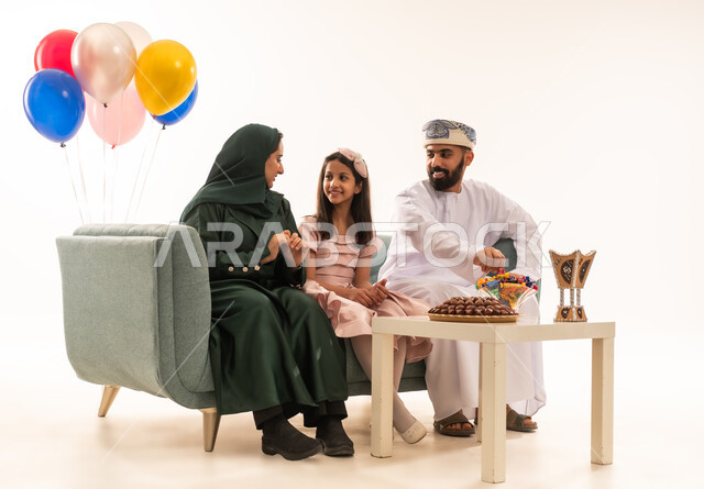 مظاهر العيد بين الأهل, الاحتفال بالأعياد الإسلامية والزيارات العائلية، تقديم الحلويات الشعبية،أجواء البهجة والسعادة في العيد، بورتريه لعائلة عربية خليجية عمانية تجلس في غرفة المعيشة وتقوم بتبادل المعايدات، مفهوم الحنان والمحبة والمودة، خلفية بيضاء .