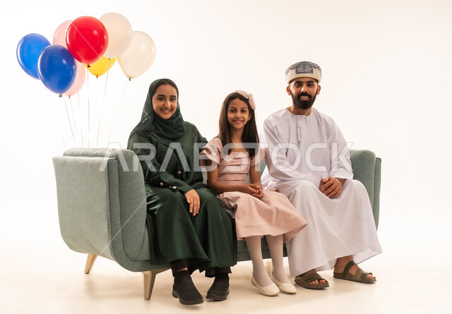 النظر الى الكاميرا بايماءات البهجة ، الاحتفال بالأعياد الإسلامية والزيارات العائلية، ضيافات الأعياد العربية الشعبية في سلطنة عمان، بورتريه لعائلة عربية خليجية عمانية تجلس في غرفة المعيشة وتقوم بتبادل المعايدات، إظهار مشاعر الفرح والسعادة بقدوم العيد، مفهوم الحنان والمحبة والمودة، خلفية بيضاء .