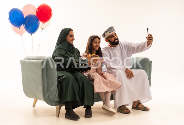 صور السيلفي التذكارية  فى العيد، الجلوس في غرفة المعيشة في جو عائلي دافئ، تجمع العائلة العمانية لاستقبال العيد المبارك, إظهار مشاعر الحنان والمحبة,  بورتريه لعائلة عربية خليجية عمانية تحتفل بالمناسبات الاسلامية برفقة بعضها البعض, ارتداء الثياب الجديدة الجميلة ، خلفية بيضاء .