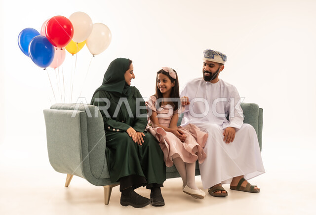 إظهار مشاعر الفرح والسعادة بقدوم العيد، الاحتفال بالأعياد الإسلامية والزيارات العائلية، ضيافات الأعياد العربية الشعبية في سلطنة عمان، بورتريه لعائلة عربية خليجية عمانية تجلس في غرفة المعيشة وتقوم بتبادل المعايدات، مفهوم الحنان والمحبة والمودة، خلفية بيضاء .