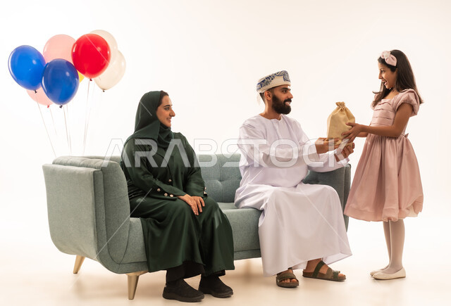 الزينة والبلالين والاحتفالات، إظهار مشاعر الفرح والسعادة بقدوم العيد، الاحتفال بالأعياد الإسلامية والزيارات العائلية، ضيافات الأعياد العربية الشعبية في سلطنة عمان، بورتريه لعائلة عربية خليجية عمانية تجلس في غرفة المعيشة وتقوم بتبادل المعايدات، مفهوم الحنان والمحبة والمودة، خلفية بيضاء .