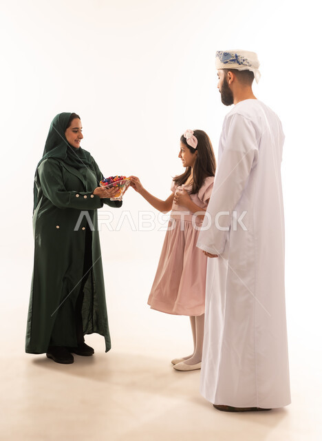 توزيع الحلويات الشعبية في الأعياد، طقوس المناسبات الاسلامية في سلطنة عمان، ارتداء الأزياء العمانية التقليدية، جو البهجة والفرح والزينة، تقديم العيديات للاطفال فى العيد ، بورتريه لعائلة عربية خليجية عمانية تحتفل بالعيد المبارك، خلفية بيضاء .