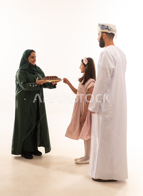 منتجات محلية وطنية ، المعايدات والتهنئات وطقوس المناسبات الاسلامية في سلطنة عمان، ارتداء الأزياء العمانية التقليدية، توزيع الحلويات الشعبية في الأعياد، جو البهجة والفرح والزينة، بورتريه لعائلة عربية خليجية عمانية تحتفل بالعيد المبارك، خلفية بيضاء .