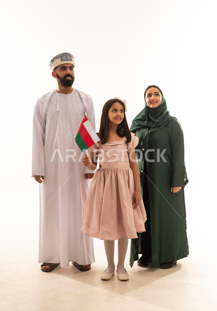 أعياد ومناسبات وطنية، إحياء ذكرى اليوم الوطني العماني، الاعتزاز والفخر بالرموز والراية العمانية، بورتريه لعائلة عربية خليجية عمانية ترتدي الملابس العمانية التقليدية ، بنت عمانية تحمل بيدها علم صغير لسلطنة عمان، مفهوم حب الوطن والإنتماء إليه، الجسم بالطول الكامل، خلفية بيضاء .