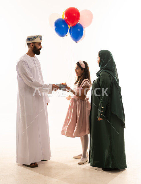 المعايدات والتهنئات وطقوس المناسبات الاسلامية في سلطنة عمان، ارتداء الأزياء العمانية التقليدية، توزيع الحلويات الشعبية في الأعياد، جو البهجة والفرح والزينة، تقديم العيديات للاطفال فى العيد ، بورتريه لعائلة عربية خليجية عمانية تحتفل بالعيد المبارك، خلفية بيضاء .