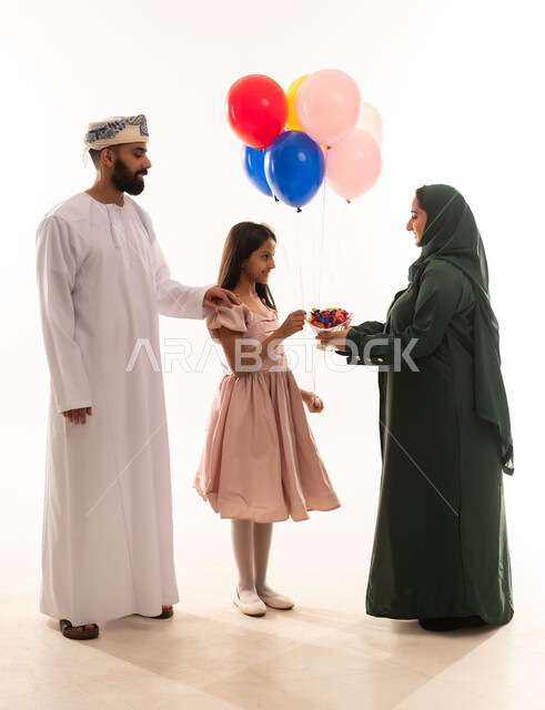التقاليد والعادات الأصيلة ، المعايدات والتهنئات وطقوس المناسبات الاسلامية في سلطنة عمان، ارتداء الأزياء العمانية التقليدية، توزيع الحلويات الشعبية في الأعياد، جو البهجة والفرح والزينة، بورتريه لعائلة عربية خليجية عمانية تحتفل بالعيد المبارك، خلفية بيضاء .
