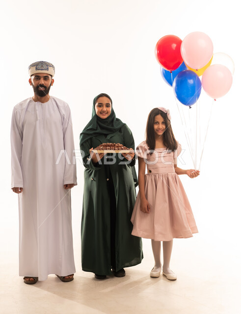 توزيعات مناسبات و استقبال فى الاعياد ، طقوس المناسبات الاسلامية في سلطنة عمان، ارتداء الأزياء العمانية التقليدية، جو البهجة والفرح والزينة، تقديم العيديات للاطفال فى العيد ، بورتريه لعائلة عربية خليجية عمانية تحتفل بالعيد المبارك، خلفية بيضاء .