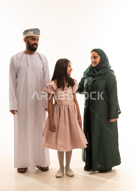 السلام والتهنئة بقدوم العيد, البلالين الملونة والزينة، إظهار مشاعر المودة والمحبة العائلية, أجواء البهجة والسعادة والاحتفال, بورتريه لعائلة عربية خليجية عمانية تحتفل بالأعياد الاسلامية, تقديم الحلويات التقليدية والمأكولات الشهية, خلفية بيضاء .