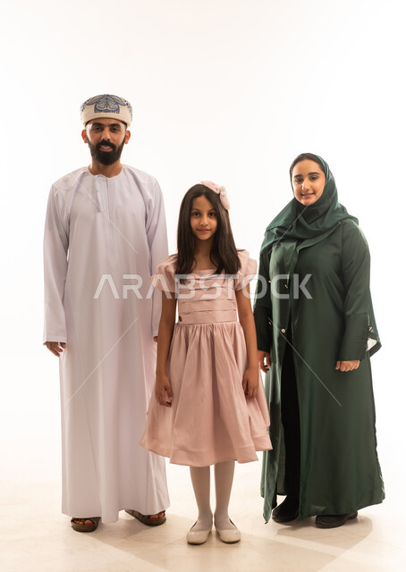 النظر الى الكاميرا بايماءات السعادة ، إظهار مشاعر المودة والمحبة العائلية, البلالين الملونة والزينة، السلام والتهنئة بقدوم العيد, أجواء البهجة والسعادة والاحتفال, بورتريه لعائلة عربية خليجية عمانية تحتفل بالأعياد الاسلامية, تقديم الحلويات التقليدية والمأكولات الشهية, خلفية بيضاء .