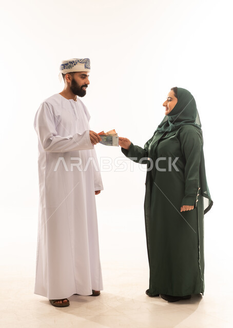 مفهوم الألفة والمحبة بين الزوجين, مشاركة وتقديم الهدايا في الأعياد والمناسبات العائلية, رجل عربي خليجي عماني يرتدي ادشداشة والكمة يقدم لزوجته العيدية بمناسبة قدوم العيد, خلفية بيضاء .