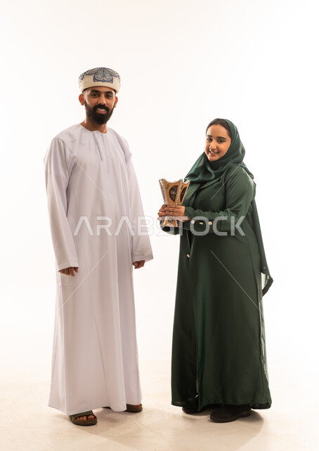 Using agarwood in social and religious occasions, perfuming and scenting, preparing to go out, portrait of a young Arab Gulf Omani woman carrying an incense holder (incense burner), an Arab Gulf Omani man wearing a dishdasha and a kummah, white background.