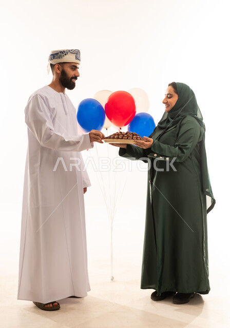 مفهوم احترام الزوج وتقديره، منتج زراعي محلي وطني ضيافة رمضانية لذيذة، افطار الصائم في رمضان، وجبة ذات قيمة غذائية عالية، بورتريه لامراة عربية خليجية عمانية ترتدي العباءة والحجاب تقوم بتقديم التمر الصحي لزوجها، الاحتفال بقدوم شهر الخير، خلفية بيضاء .