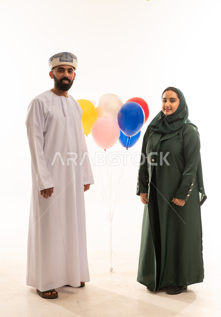 طقوس الاحتفالات والمناسبات السعيدة في سلطنة عمان، ارتداء الأزياء العمانية التقليدية، جو البهجة والفرح والزينة، بورتريه لزوجان عربيان خليجيان عمانيان يحتفلان بالعيد المبارك، كرم الضيافة وحسن الاستقبال ، توزيع الحلويات الشعبية في الأعياد، خلفية بيضاء .
