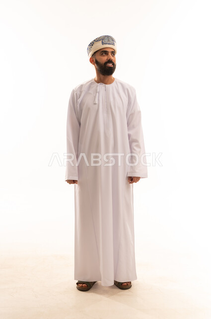 إيماءات السرور والبشاشة لتحديد موقع معين ، بورتريه لرجل عربي خليجي عماني مبتسم يرتدي الدشداشة والكمة ينظر نحو الأعلى إلى شيء ما، الاهتمام بالأناقة والمظهر الخارجي، صورة الجسم بالطول الكامل، خلفية بيضاء .