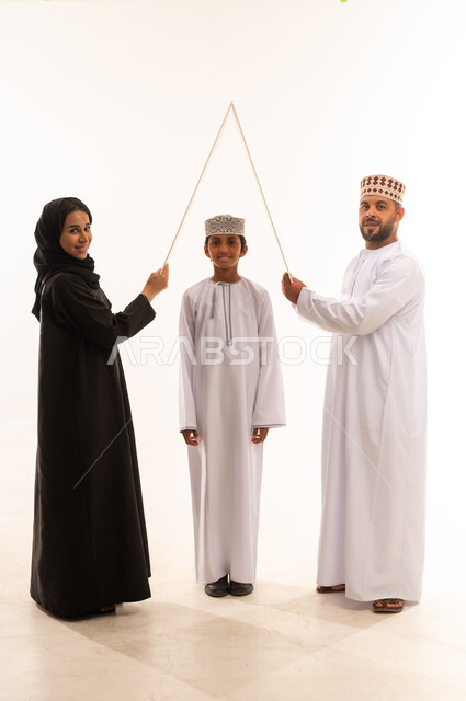 Gestures indicating happiness, family stability in housing and ownership, meeting family household needs, portrait of an Omani Gulf Arab couple holding a white board over the son's head, spending time with family and children, white background.