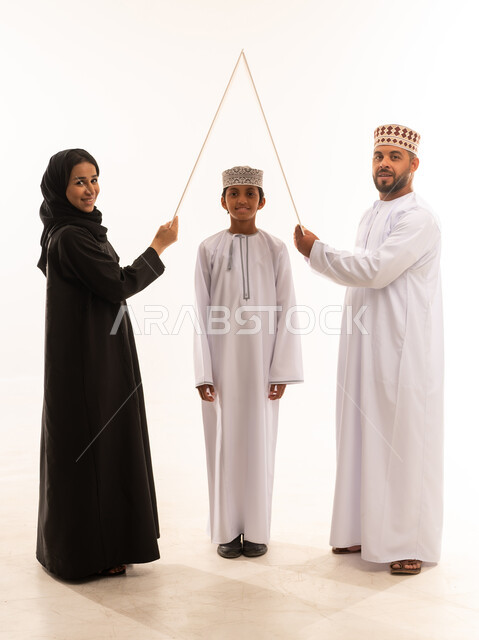 تلبية الاحتياجات المنزليه العائلية، ايماءات تدل على السعادة, الاستقرار العائلي في الاسكان والتمليك ،بورتريه لزوجان عربيان عمانيان خليجيان يحملان لوح أبيض فوق رأس الابن , قضاء الوقت مع الأهل والأبناء ، خلفية بيضاء .