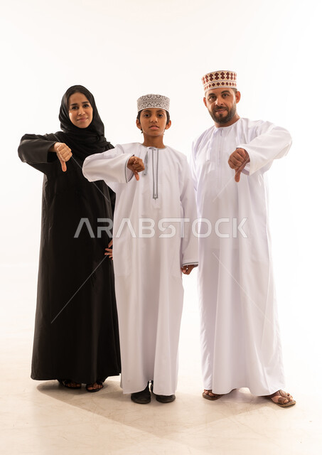 حركة يد وايماءات وجه تدل على عدم الإعجاب والموافقة، الشعور بالإنزعاج من شيء ما، الاهتمام بالأبناء ورعايتهم، بورتريه لعائلة عربية خليجية عمانية يرتدي الملابس العمانية التقليدية تنظرالى الكاميرا ، تعزيز العلاقات الاجتماعية، الجسم بالطول الكامل، خلفية بيضاء .