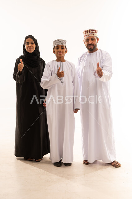 رفع اصابع الابهام للاعلى بعلامة الجودة ، ايماءات الاعجاب والقبول، الاهتمام بالأبناء ورعايتهم، بورتريه لعائلة عربية خليجية عمانية يرتدي الملابس العمانية التقليدية تنظرالى الكاميرا ، تعزيز العلاقات الاجتماعية، الجسم بالطول الكامل، خلفية بيضاء .