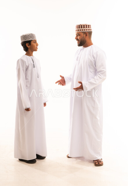 الرقي في التعامل وتبادل الأحاديث،أجواء أسرية مليئة بالمودة، بورتريه لأب وابنه عربيان خليجيان عمانيان يرتديان الدشداشة والكمة ، ارتداء الملابس العمانية التقليدية في الأعياد الإسلامية، خلفية بيضاء .