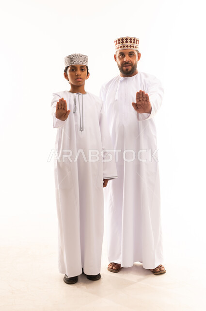 الأمر بالتوقف عن فعل شيء ما، تعابير الرفض والإمتناع, الرابطة الأبوية والترابط الأسري، ايماءات الحب والعطف على الأبناء، بورتريه لأب وابنه عربيان خليجيان عمانيان يرتديان الدشداشة والكمة ، ارتداء الملابس العمانية التقليدية في الأعياد الإسلامية، خلفية بيضاء .