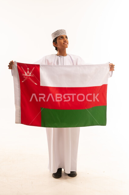 الاحتفال بذكرى اليوم الوطني العماني، الاعتزاز والفخر بالرموز والراية العمانية، المشاركة بالاعياد والمناسبات الوطنية، بورتريه لولد عربي خليجي عماني يرتدي الدشداشة والكمه، مفهوم حب الوطن والإنتماء إليه، الجسم بالطول الكامل، خلفية بيضاء .