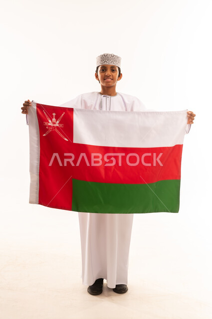 Participating in national holidays and occasions, celebrating Omani National Day, pride in Omani symbols and flag, portrait of an Omani Gulf Arab boy wearing a dishdasha and a kuma, the concept of patriotism and belonging to the homeland, full body, white background.