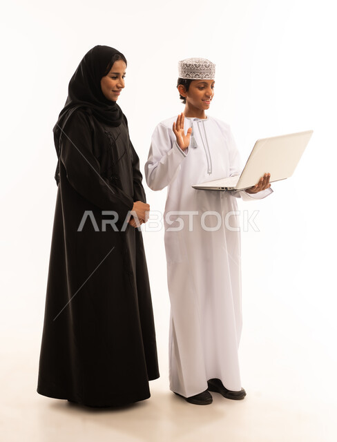 تشجيع الأبناء والاعتناء بهم، متابعة حصص الاونلاين عبر جهاز الحاسوب المحمول، بورتريه لولد عربي خليجي عماني بجانب والدته يقوم بالتعلم عن بعد بإيماءات الضحك و السعادة، أخبار جديده على مواقع التواصل الاجتماعي، صورة الجسم بالطول الكامل، خلفية بيضاء .
