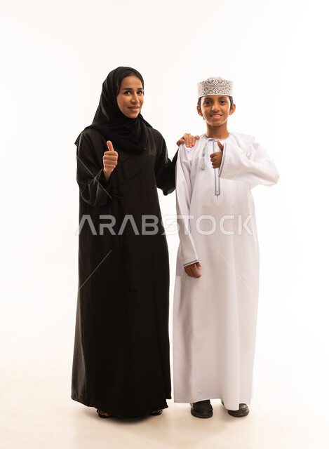 رفع اليد بعلامات الجودة والامتياز، ارتداء الملابس العمانية التقليدية في الأعياد الإسلامية، ايماءات الحب والعطف على الأبناء، حب الأم لأولادها ,الامومه والترابط الأسري، بورتريه لأم وابنها عربيان خليجيان عمانيان يرتديان الزى العماني يتبادلان الحديث ، خلفية بيضاء .