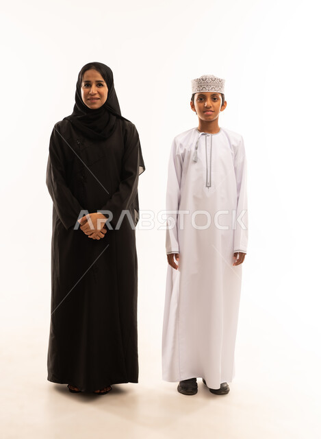 ايماءات الحب والعطف على الأبناء، حب الأم لأولادها ,الامومه والترابط الأسري، بورتريه لأم وابنها عربيان خليجيان عمانيان يرتديان الزى العماني ، ينظران الى الكاميرا بايماءات السعادة ، ارتداء الملابس العمانية التقليدية في الأعياد الإسلامية، خلفية بيضاء .