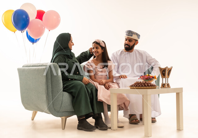 الزيارات العائلية والاحتفال بالأعياد الإسلامية، تقديم الضيافة العربية والحلويات الشعبية، بورتريه لعائلة عربية خليجية عمانية تجلس في غرفة المعيشة وتقوم بتبادل المعايدات, إظهار مشاعر الفرح والسعادة بقدوم العيد، مفهوم الحنان والمحبة والمودة، خلفية بيضاء .