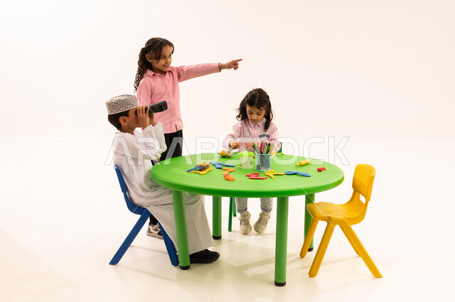 Future outlook of boys, gestures of happiness and surprise, portrait of an Arab Gulf Omani boy wearing a kummah and a dishdasha, zooming in on distant objects through a telescope next to his girlfriend, using binoculars, pointing at something, love of exploration and adventure, white background
