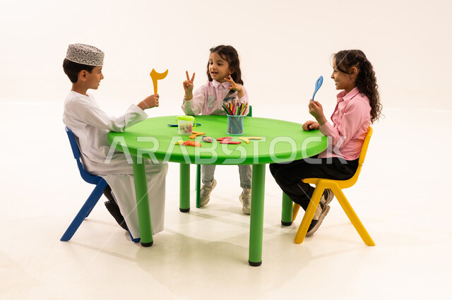 Learning Arabic numbers and figures and their shapes, a portrait of an Arab Gulf Omani boy wearing a dishdasha and a kuma learning arithmetic with his friends, recreational and educational activities that help develop intellectual abilities, cooperation and participation among kindergarten children in learning mathematics, white background
