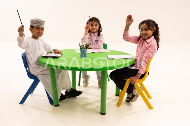 تعزيز المهارات الفنية بالرسم والتلوين، الجلسات والحصص التعليمية في الروضات العمانية، بورتريه لفتى عربي خليجي عماني يرتدي الكمة والدشداشة يقوم بتلوين الرسومات بايماءات الاندماج مع اصدقاءه، القيام بالمهارات و الأنشطة المختلفة لتنمية القدرات العقلية والذهنية، خلفية بيضاء